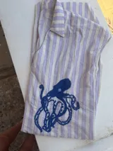 Túnica de lino a rayas verticales color lila y blanco, con cuello polo y bordado de un pulpo azul en el frente.
