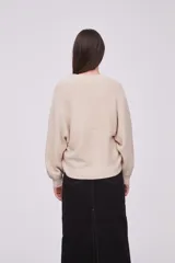 Sweater color beige con diseño de cruz y manga larga, tejido suave.