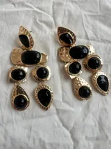 Aros colgantes dorados con apliques de piedras negras de diferentes formas.