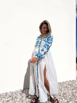 Túnica playera blanca traslúcida con bordados azules, mangas largas y abertura frontal.