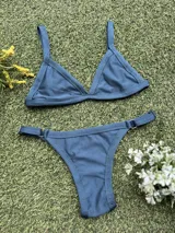 Conjunto de bikini color petróleo, de lycra acanalada, compuesto por un corpiño de triángulo fijo con breteles regulables y una bombacha colaless regulable con argollas metálicas.