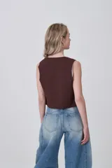 Chaleco sin mangas color marrón oscuro, de corte ajustado al cuerpo, con escote en V y cierre frontal mediante lazos anudados con detalles de cuentas oscuras.