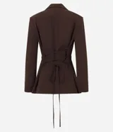 Blazer sastre color marrón, de corte alargado y ligeramente entallado. Presenta cuello solapa clásico, cierre frontal con un solo botón y forro interno. Las mangas son largas y en la espalda tiene un recorte central con tiras ajustables entrelazadas para un lazo personalizado.