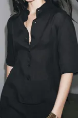 Camisa negra de manga corta confeccionada en hilatura con lyocell y ramio, con cuello solapa, bajo recto y cierre frontal con botones.