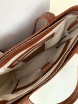 Cartera tipo tote de cuero graneado color negro, con textura uniforme y suave al tacto. Tiene manijas de 55 cm, bolsillo frontal con broche imantado, bolsillo trasero con cierre metálico, cierre principal metálico, forro interior y tres bolsillos internos (uno con cierre, uno plaqué y uno tipo sobre con solapa y botón).