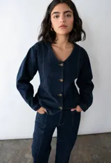 Camisa entallada de denim azul oscuro con cuello en V y cierre frontal con botones. Confeccionada en algodón reciclado con espalda ajustable.