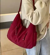 Bolso hobo color bordó de tela suave, liviana y espaciosa, con bolsillos frontales con cierre y correa ajustable.