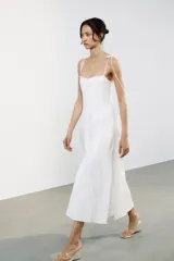 Vestido midi blanco de popelín con escote corazón y volantes. Tiene tirantes finos con detalle de lazo, forro interior combinado y cierre lateral con cremallera oculta.