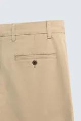Pantalón chino color beige, de corte recto y tiro medio. Confeccionado en tejido de algodón con elasticidad, con bolsillos laterales y traseros de vivo. Cierre frontal con cremallera y botón.