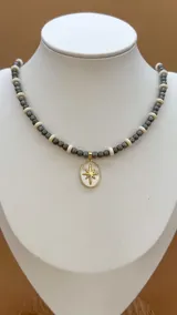 Collar de cuentas grises y blancas con dijes dorados con incrustaciones de circonitas.