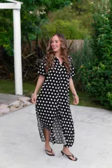 Camisola larga de muselina negra con estampado de lunares blancos, cuello camisero y manga corta. Presenta un corte holgado y abotonadura frontal completa.