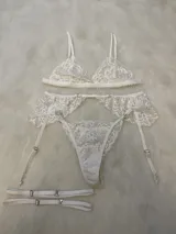 Conjunto de lencería de encaje color bordó, compuesto por un corpiño tipo bralette con breteles regulables, una tanga regulable con corte media less y un portaligas con volados y ligas incluidas.