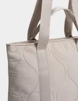 Bolso tipo shopper color beige, con diseño acolchado y pespuntes ondulados. Tiene doble asa de hombro y correa extraíble regulable.