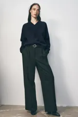 Pantalón negro de tiro alto con pinzas delanteras, pernera ancha y cinturón de cuero con hebilla dorada.