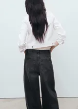 Chaqueta de jean blanca con cuello camisero, bolsillos de parche con solapa en el pecho, cierre frontal con botones y mangas largas con puños abotonados.