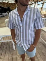 Camisa de manga corta con rayas verticales grises y blancas, cuello americano y botones marrones.