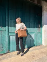 Bolso tipo tote de cuero color camel con forro de tela, doble asa corta y bolsillo frontal con cierre.