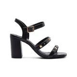 Sandalia negra de taco alto con tiras finas y apliques de tachas doradas.