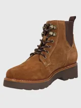 Bota de gamuza color tostado con cordones frontales y paneles elásticos laterales. Presenta una suela de goma gruesa con costuras decorativas, ojales metálicos y tirador trasero para facilitar el calce.