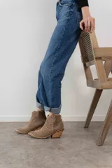 Bota corta de gamuza color marrón oscuro, con puntera cuadrada y detalles de costuras decorativas. Tiene un taco de madera con forma cónica.