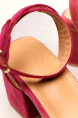 Sandalia de terciopelo verde con taco cuadrado de 7 cm, punta cuadrada y tiras anchas anudadas en el empeine. Cuenta con una tira fina ajustable al tobillo con hebilla dorada.