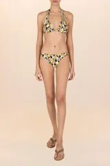 Calzón de bikini de corte a la cadera con cobertura pequeña. Presenta un estampado abstracto en tonos mostaza, negro y blanco, con un diseño que simula hojas o manchas. Es reversible, ofreciendo un segundo look.