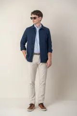 Sobre camisa color beige confeccionada en lino, de corte recto, con cuello clásico, manga larga con puños abotonados, cierre frontal con botones a tono, bolsillo de parche en el pecho y ruedo recto.