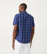 Camisa de manga corta con estampado de cuadros azules y blancos, cuello camisero y abotonadura frontal.