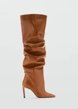 Bota de cuero color marrón con detalle fruncido, caña alta, punta fina y tacón de aguja de 7cm.