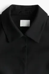 Campera corta negra con cuello clásico, hombros ligeramente caídos, bolsillos decorativos delanteros y forro interior.