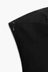 Top negro palabra de honor con escote recto y detalle de pieza metálica en forma de V forrada. Tiene falsos bolsillos con solapa en el delantero, forro interior combinado y cierre lateral con cremallera oculta.