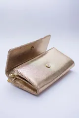 Cartera tipo sobre color beige con textura granulada y correa de cadena dorada.