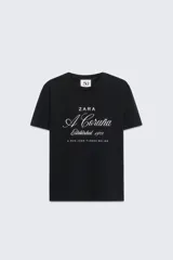 Camiseta marrón de algodón con cuello redondo y mangas cortas. Estampado frontal con el texto "Zara A Coruña Established 1975 A Rúa Juan Flórez 64-66" en color blanco.
