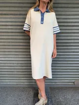 Vestido midi color crudo, tejido en hilo, con cuello polo azul y mangas cortas con rayas azules.