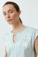 Remera de manga corta color verde agua con bordado floral blanco en la zona del pecho y cuello con abertura en forma de lágrima.