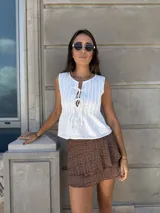 Top blanco sin mangas con cuello redondo y abertura frontal con lazos ajustables. Presenta textura de pliegues verticales en el frente.