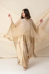 Poncho artesanal color beige con hilos de lurex dorados y terminación de flecos. Diseño irregular, más corto adelante que atrás.