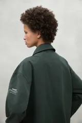 Chaqueta color beige, repelente al agua, con cuello clásico, cierre con botones, bolsillos laterales y corte holgado. Fabricada con poliéster reciclado y algodón orgánico.