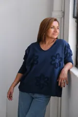 Remera azul marino de corte holgado, con cuello en V y mangas 3/4. Presenta apliques de flores en relieve en el frente y las mangas.