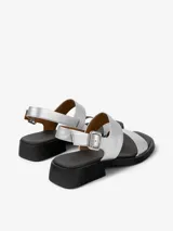 Sandalias plateadas de cuero vacuno con dos tiras anchas sobre el empeine, tira trasera con hebilla ajustable y suela negra con pequeño taco cuadrado.