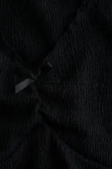 Top corto negro en punto suave con efecto arrugado, escote de pico con moño de satén y costura fruncida.