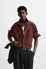 Camisa color borgoña de corte relajado, confeccionada en tejido con mezcla de viscosa. Tiene cuello solapa, manga larga con puños abotonados, bolsillo de parche en el pecho y cierre frontal con botones.