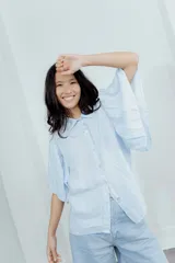 Camisa celeste de lino con cuello clásico, mangas cortas acampanadas y cierre frontal con botones.