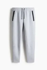 Pantalón de jogging deportivo color gris claro, de corte ajustado (slim fit), confeccionado en tejido funcional DryMove™ que absorbe el sudor. Presenta cintura elástica con cordón de ajuste negro y bolsillos laterales con cierre sellado negro.