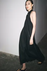 Vestido midi negro de lino, con cuello halter, hombros descubiertos, espalda descubierta, cierre frontal con botones y bajo asimétrico.