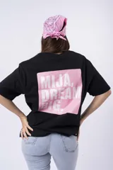 Remera negra de corte oversize con estampado frontal que dice "MIJA DREAM BIG" en tipografía blanca y rosa.