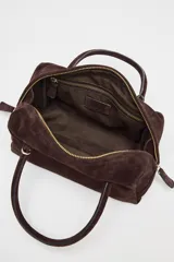 Bolso formato bowling color marrón chocolate, confeccionado en serraje. Tiene doble asa de mano y correa bandolera extraíble. Incluye bolsillo interior con cremallera y cierre principal con doble cremallera con tirador.