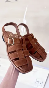 Sandalias de cuero marrón con diseño de tiras entretejidas y hebilla lateral.