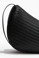 Cartera bandolera negra con diseño trenzado, forma asimétrica, cierre superior y correa ajustable.