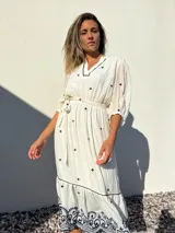 Vestido largo blanco con bordados azules, escote en V, mangas 3/4 abullonadas y lazo en la cintura.